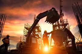 Silhouetted image of three construction workers standing in front of a construction site at sunset.